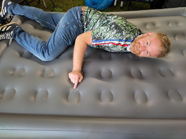 A photo of a man lying on an inflatable mattress pointing to a repaired hole.